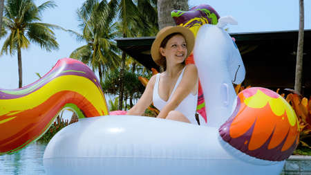 Happy traveler tourist in swimwear and hat relaxing on inflatable unicorn toy at holiday at luxury...
