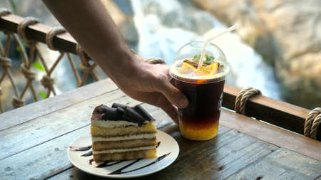 Man hand take away plastic cup with cold orange coffee. Iced coffee to go in outdoor cafe with...