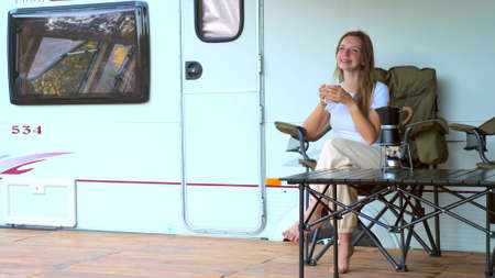 Happy young woman drinking coffee at door of a camper RV van motorhome