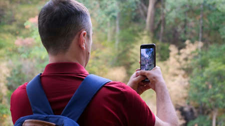 Male traveler blogger with backpack in nature filming video on smartphone camera
