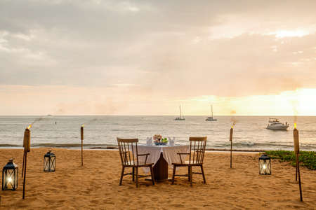Romantic sunset dinner on beach. Table honeymoon set for two with luxurious food, glasses of...