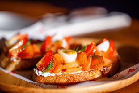 Close up of salmon toast starter or appetizer with egg and tomato on sun light. Bread slice with...