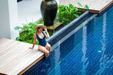 Young woman in swimwear sitting at poolside, enjoy summer vacation in tropical resort. Female travel...