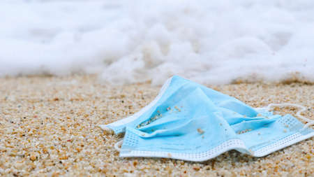 Waste pollution at the sea beach since coronavirus COVID-19 pandemic. Used face mask floating washed away by ocean wave water at coastline. Environmental and ocean pollution during coronavirusの写真素材