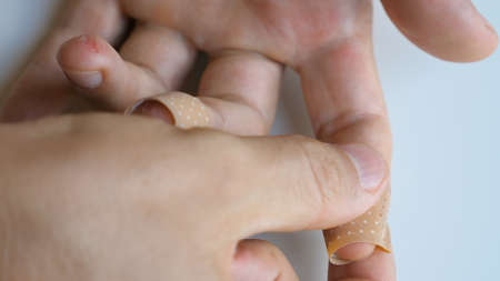 Man putting medical adhesive bandage tape sticking plaster on cuts wound on finger. Male applying...