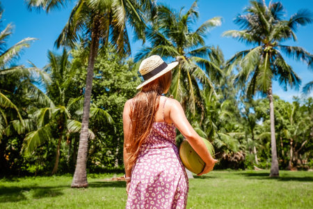 Back view of travel women over exotic tropical green palm trees and blue sky background. Summer vacation. Girl in straw hat relaxing on travel vacation in summer sun on Thailand islandの写真素材