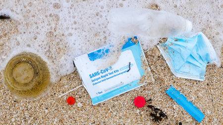 Plastic bottle, trash, face mask and Covid test on a sandy sea beach