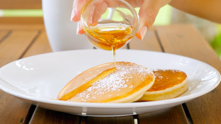 Woman hands pouring maple syrup on buttermilk pancakes