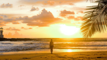 Young woman stands on edge of sea waves in romantic golden sunset lights. Happy girl enjoy summer vacation holidays at ocean. Female tourist walking barefoot at seaside on sandy beach. Slow motionの写真素材