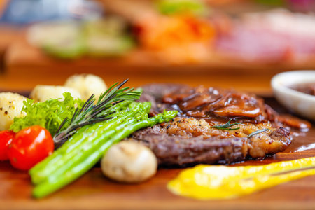 Delicious ribeye beef steak with grilled vegetables on wooden board.の写真素材