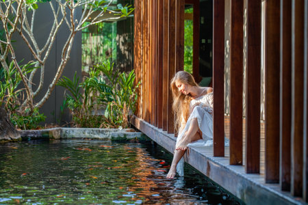 Woman in white dress relaxing at luxury spa with fish pondの写真素材
