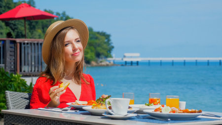 Woman sitting at table in restaurant with sea viewの写真素材