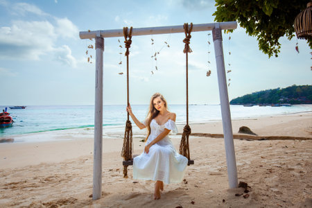 Woman enjoying swing above shore on tropical island.の写真素材