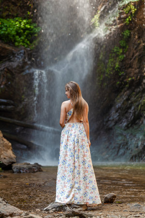 Woman in dress, tropical waterfall backdrop.の写真素材