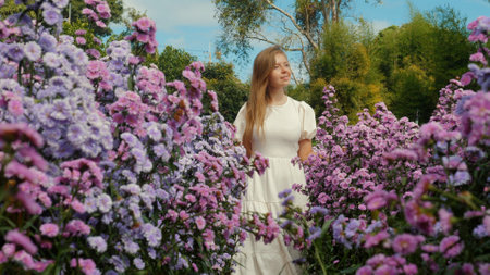 Woman with long hair in dress walks among vibrant purple wildflowersの写真素材