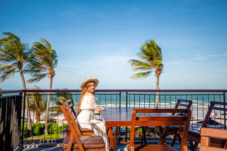 Woman in white dress with straw hat enjoying coastal viewの写真素材
