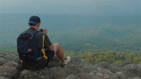 Solo Traveler Sitting on Rocky Cliff, Capturing Scenic Mountain Viewの写真素材