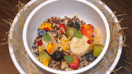 Vibrant bowl of mixed fruit salad with quinoa, garnished with edibleの写真素材