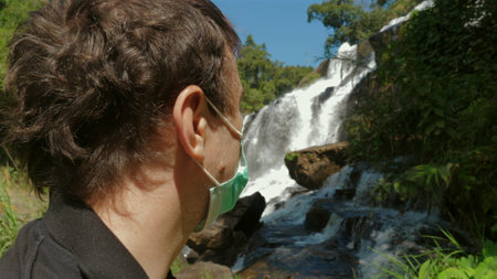 Man Wearing Mask Admiring Waterfall in Nature, Social Distancing.の写真素材