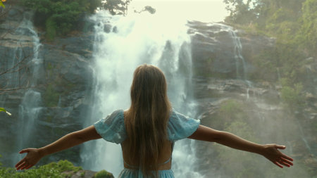 Young woman in blue dress stands with outstretched arms facingの写真素材