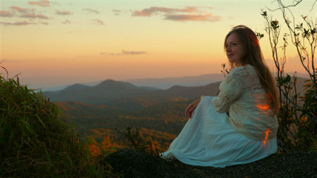 Woman Sitting on Rock Overlooking Scenic Mountain Landscape at Sunset,の写真素材