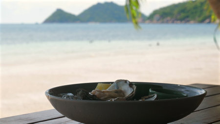 Seafood platter on wooden table overlooking serene beach with islandの写真素材