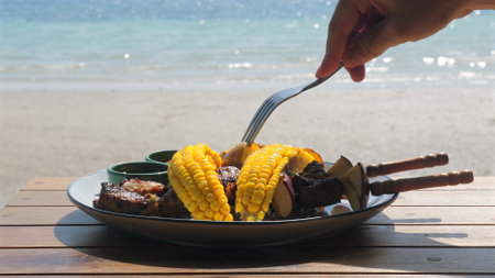 Person eating grilled corn and skewers by seaside, capturing casualの写真素材