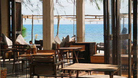 Cozy beachside restaurant with wooden furniture and scenic ocean view,の写真素材