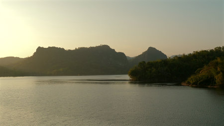 Serene lake at sunset with mountains and forested areas in background,の写真素材