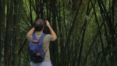 Man with backpack taking photo in dense bamboo forest, capturing
