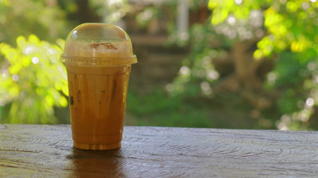 Iced coffee in plastic cup on wooden table with blurred green natureの写真素材