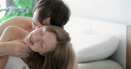 Couple in tender embrace on bed, bright airy bedroom setting, intimateの写真素材