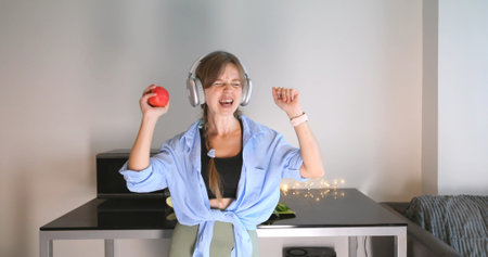 Woman enjoying music, holding apple, wearing headphones in casual homeの写真素材