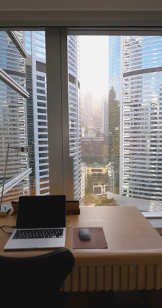 Modern office desk and laptop facing panoramic skyscraper view in
