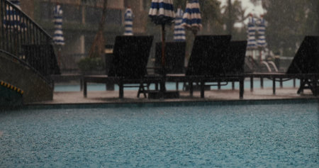 Rainy day at outdoor swimming pool with loungers and umbrellas,の写真素材