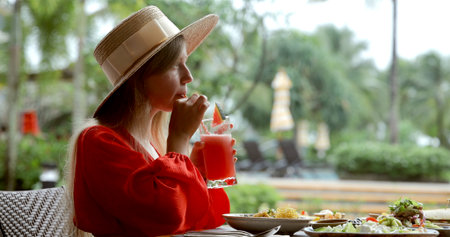 Young woman in summer hat enjoying tropical drink at outdoor cafe.