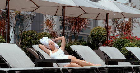 Woman sunbathing on rooftop lounge chair, relaxing under umbrellasの写真素材