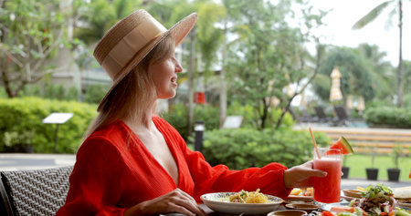 Woman in red dress enjoying refreshing tropical drink at outdoor cafe.