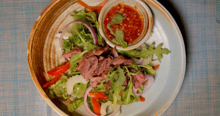 Grilled beef salad with red onion, arugula, and spicy dipping sauce on
