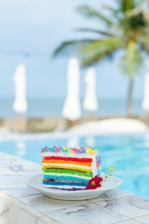 Colorful rainbow cake slice by tropical pool, creating vibrant summerの写真素材