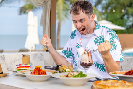 Excited man enjoying diverse dishes at outdoor beach restaurant.の写真素材