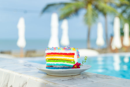 Colorful rainbow cake by pool at tropical resort, vibrant dessert withの写真素材