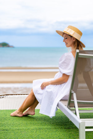 Woman relaxing on beach chair, wearing sunhat, enjoying coastalの写真素材