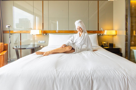 Relaxed woman in hotel room wearing bathrobe, sitting on largeの写真素材