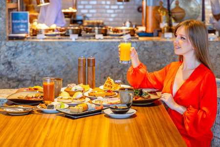 Woman enjoying breakfast buffet in restaurant, holding orange juice.の写真素材
