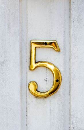 Golden number five on white wooden wall
