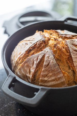 Freshly baked sourdough bread in a black cast iron Dutch oven. The rustic golden crust features an...