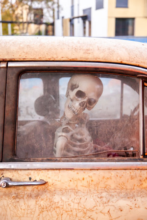 Close up photo of a human skeleton model sitting inside an old rusted car seen through a dirty...