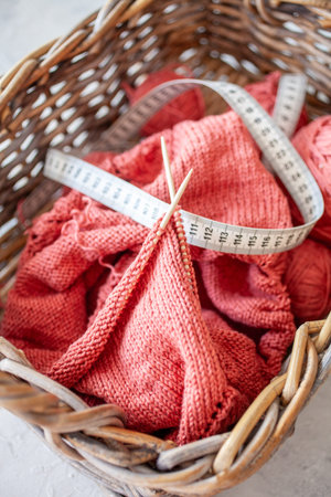 Close up photo of a knitting project in a basket with soft yarn wooden needles and a measuring tape...