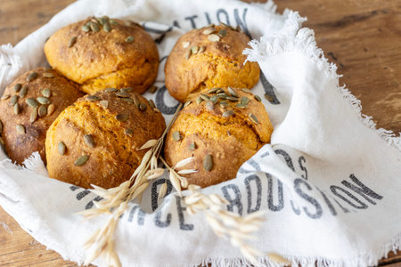 The image shows golden-brown carrot bread rolls topped with pumpkin seeds, arranged in a wicker...